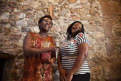 Two women laughing and standing against a stone wall.