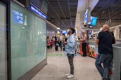 Afghan refugee Mehdi, 29, looks up at a bank of flight arrival monitors for his brother's flight status.