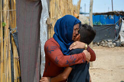 A Syrian woman hugs her son outside at a refugee camp.