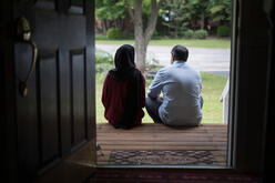 Resettled couple sits in the doorway of their new home