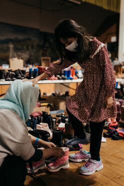 A woman helps a young girl put on winter boots at the IRC's winter clothing drive.