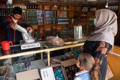 A man weights food while Noor and her daughter look on in an outdoor market in Afghanistan.