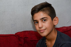 A headshot of 13-year-old Yasser as he sits on a sofa