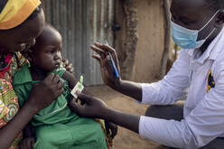 Anan holds her son while a doctor fits an armband around his arm. It shows green, meaning the child has recovered.