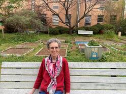 Sue Binder, sitting on a bench in front of the Clarkston High School garden.