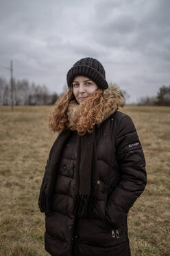 Anastasiia stands in a field wearing winter clothes 