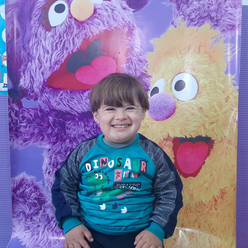 Saeed, a 5-year-old Syrian boy with Down's Syndrome, stands grinning in front of a Sesame Street poster.