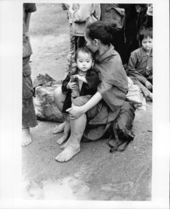 A refugee woman and child from Laos sit on the ground outside, awaiting medical treatment.