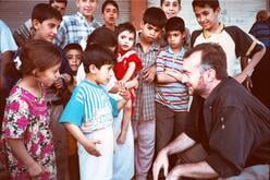 A middle aged man squats down as he talks with a group of Iraqi children.