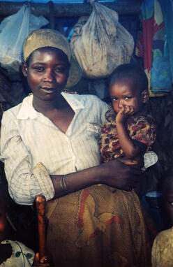 An Angolan woman stands and holds a small child as they look at the camera.