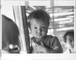 A young girl from Southeast Asia looks at the camera with a serious expression.