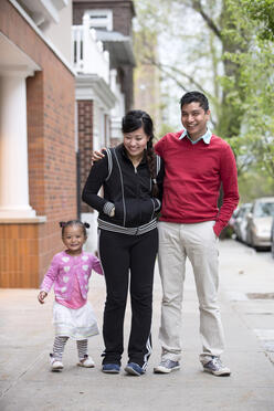 A family of 3 walking down a sidewalk.