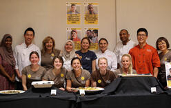Staff members and chefs of the Spice Kitchen Incubator sit and stand behind a table with smiles.