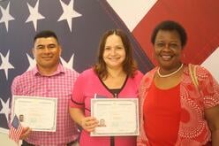 Three people smiling for a picture while holding citizenship certificates.