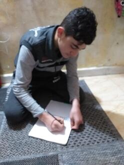 13 year old Alaa draws on paper whilst sitting on the floor. 
