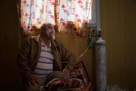 Abu Raed often relies on an oxygen mask to treat his asthsma. Abu Raed sits by a window in his caravan, wearing an oxygen mask.