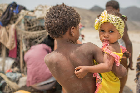 A young boy displaced by the civil war in Yemen stands with his baby sister outside a makeshift shelter