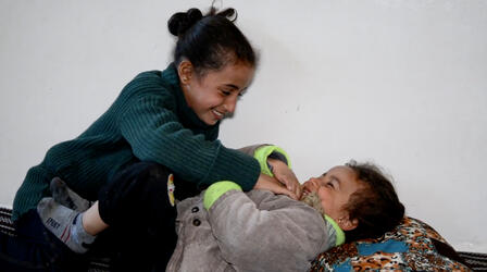 8-year-old Reem, smiling, plays with her giggling little sister Layla in Syria.