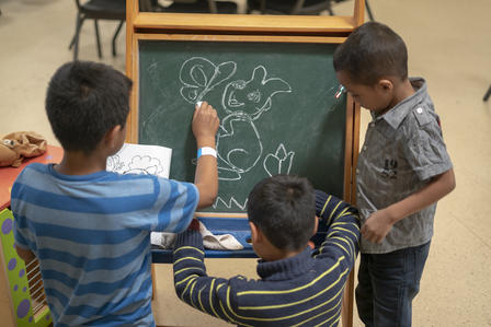 Three boys draw a rabbit on a chalkboard in the children's room