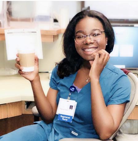 Torbertha Torbor, a nurse practitioner and refugee Torbertha Torbor poses sitting down in her scrubs. She is holding a cup of coffee and smiling.