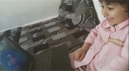 Roaa, a 3-year-old girl in Tripoli, Lebanon, Watches Ahlan Simsim on a laptop. She is smiling and looking at the screen. 