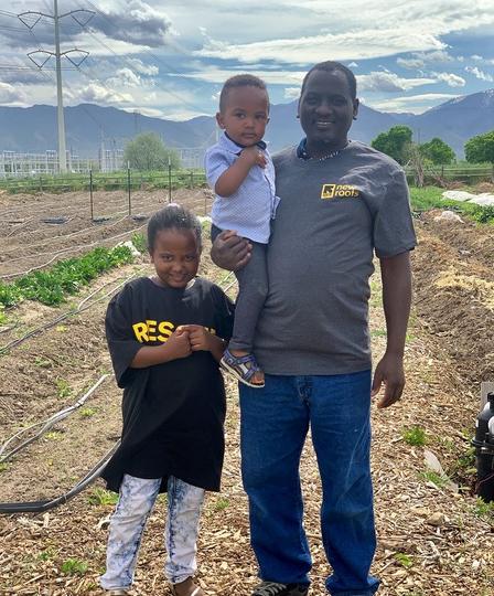 Hawaa and her family work at the Draper farm even while fasting. Family standing amidst farm land with mountains in the background.