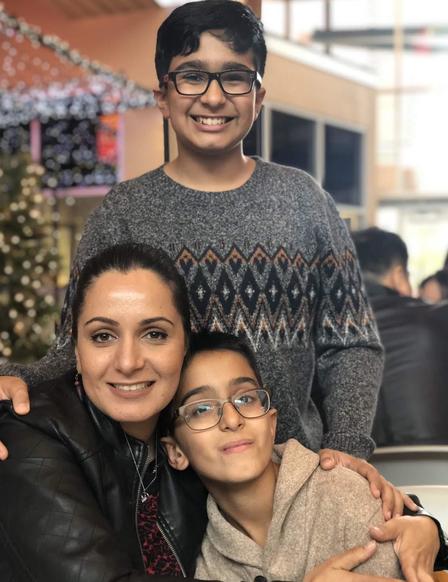 Meheria Habibi has her arm around one of her sons while another one of her sons stands behind her. All three are smiling and looking at the camera. 