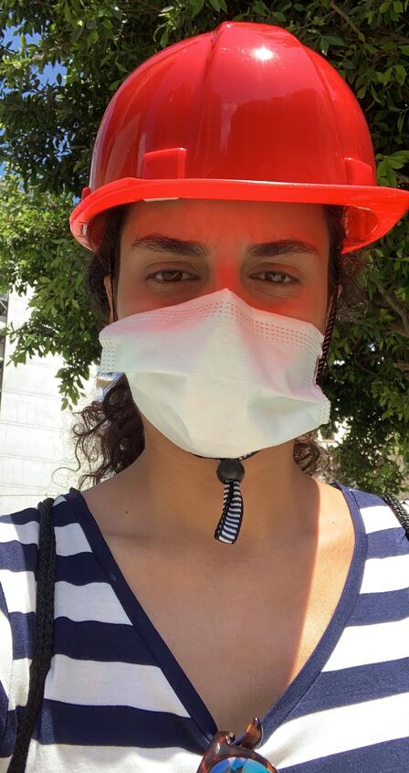 Rebecca Mouawad A selfie photo taken by Rebecca Mouawad. She is wearing a red hard hat and a white surgical mask.