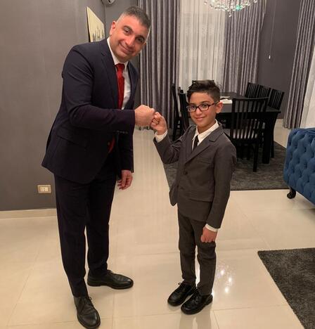 Maha's eldest son and grandson Maha's eldest son and 13-year-old grandson, both wearing suits and ties, fist bump and smile for the camera.