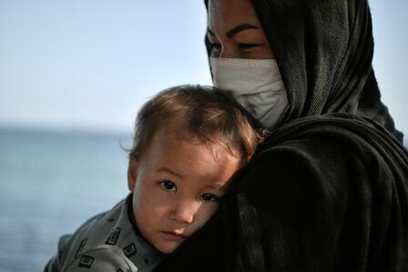 A mother and child in Greece after fleeing for safety across the Mediterranean Sea. Photo: L. Gouliamaki/IRC A mother wearing a face mask holds her baby in a refugee settlement in Greece