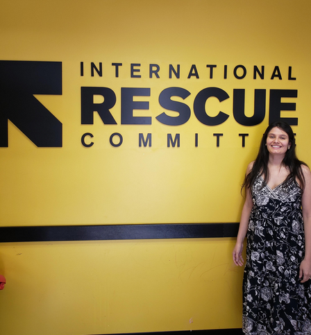 The IRC in Atlanta welcomed Marielys Padua Soto, B.S., J.D. to the Community Integration and Immigration Services team in September 2020. A woman in a long dress with long dark hair stands in front of a yellow wall that has International Rescue Committee in bold black letters. She is smiling.