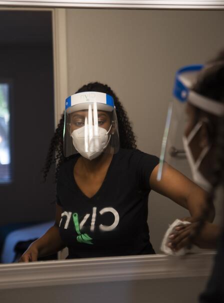 Diana in PPE cleaning Diana cleans a window while wearing a shirt with the name of her app, Clyn, as well as a face shield and mask.