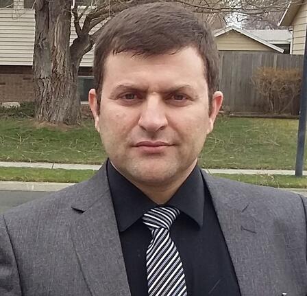 Shafi, wearing a suit and a tie, offers a slight smile as he looks at the camera