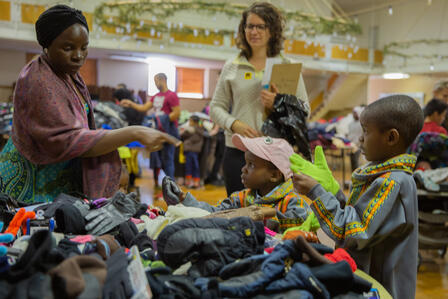 Winter Clothing drive in 2019 A mother and two children select winter accessories from a pile of gloves at the IRC's Warm Welcome Winter Clothing Drive, as the volunteer assisting them stands in the background.