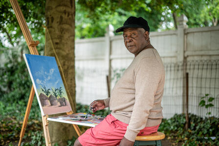Artist Muyambo Marcel Chishimba paints a landscape at his easel in his New Jersey backyard. 