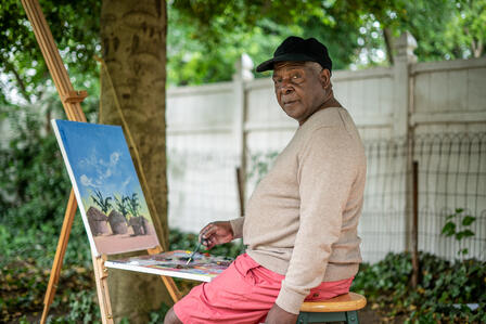 Congolese artist Muyambo Marcel Chishimba works in his backyard at an easel. Artist Muyambo Marcel Chishimba paints a landscape at his easel in his New Jersey backyard.