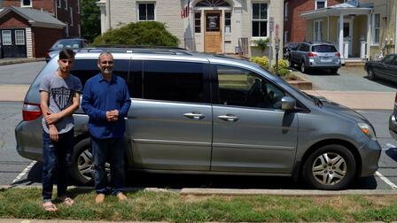 Proud family with new minivan Two men stand in front of a silver minivan they have just received