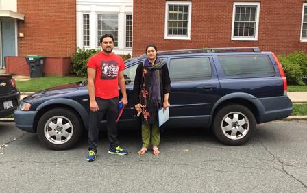 A man and woman stand in front of a black station wagon