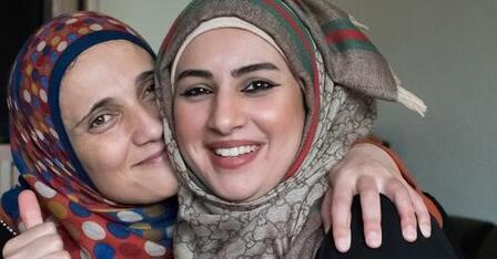 Two women from Afghanistan are smiling as they have their heads nestled against each other.