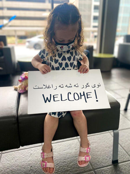 Child holds sign that says welcome to greet refugee arrivals