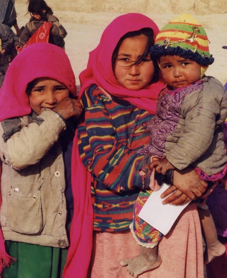 Three young Afghan girls in bright pink clothing pose for a picture.
