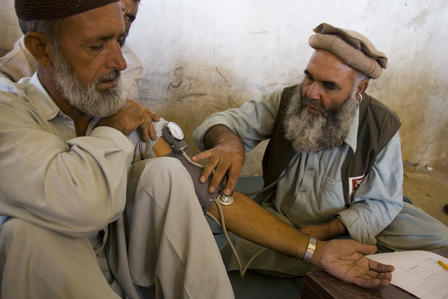 Pakistan medical care 2005 A doctor and another man, both Pakistani, sit on the floor, as the doctor takes the blood pressure of the other man.