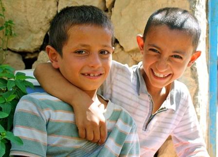 Two young Iraqi boys smile and pose for a photo, with one placing his harm around the other.