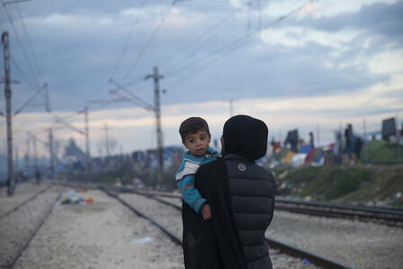 A refugee woman holds a small boy in a refugee settlement in Greece.