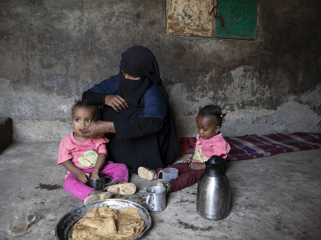 A mother siting  on the floor feeding her two children.