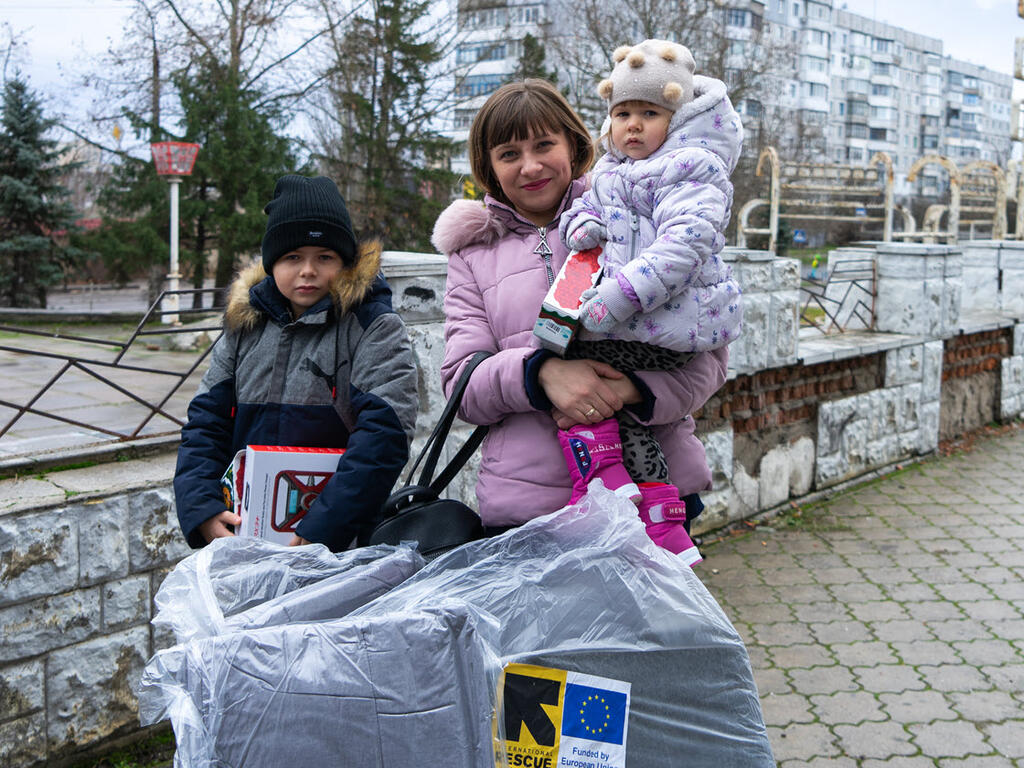 Yulia and her two children in Ukraine, bundled in winter clothes and holding large bags of winter supplies from the IRC.