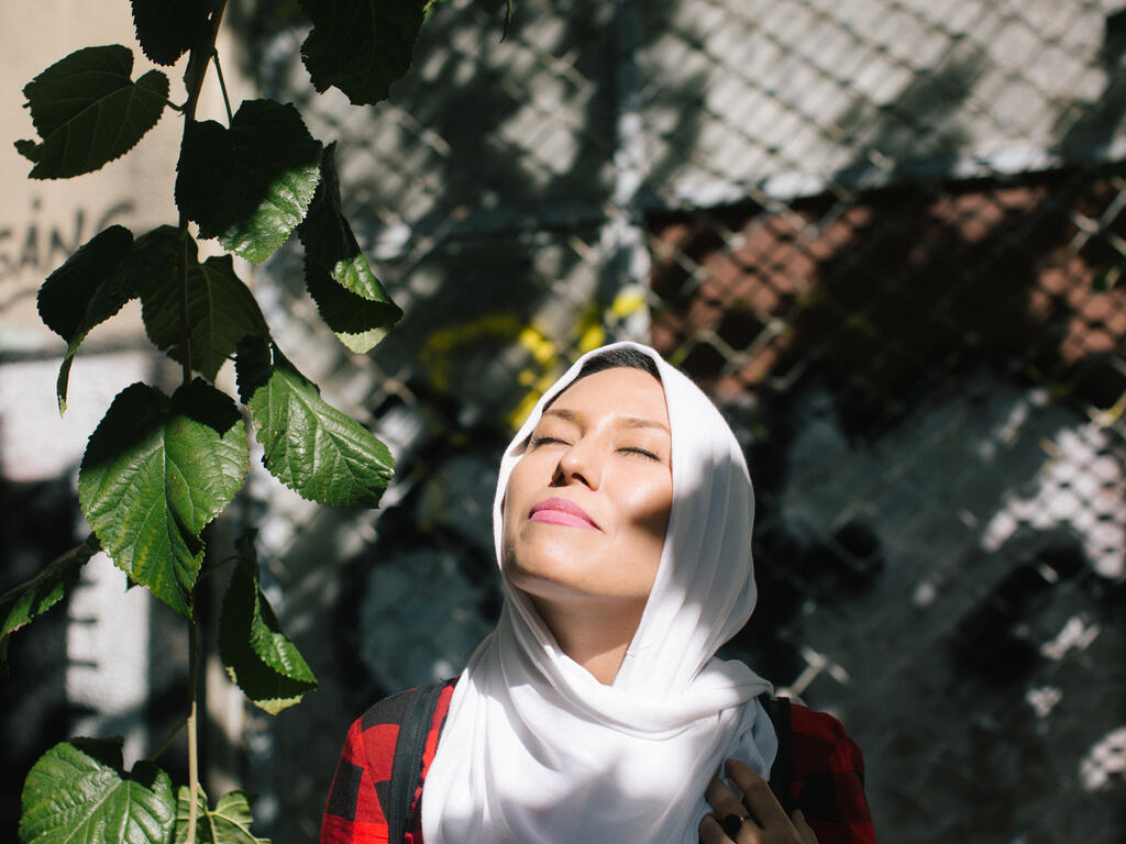 Fariba, an Afghan refugee, standing in the sunlight looking happy