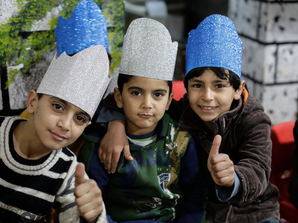 At an IRC children’s center in Syria, three boys give a thumbs up while wearing colorful handmade glitter crowns.