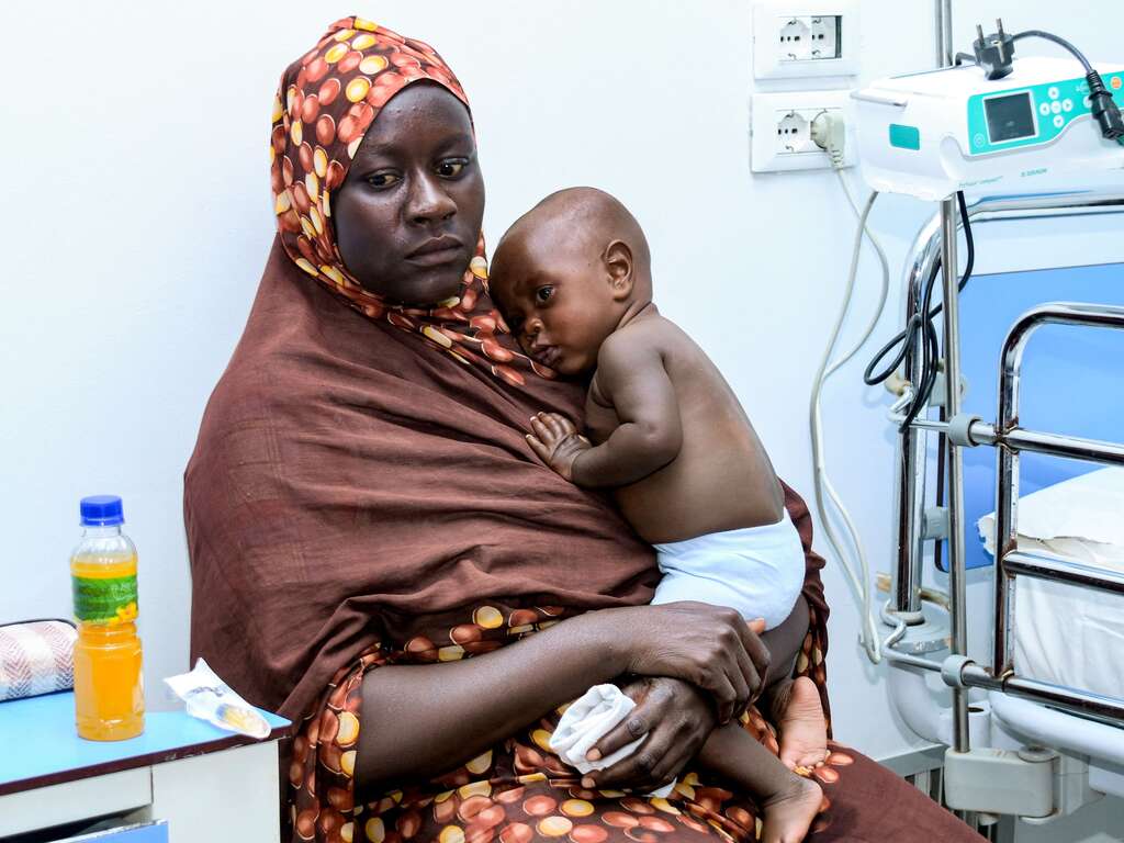 A woman waits with a child for medical care at a hospital in Port Sudan