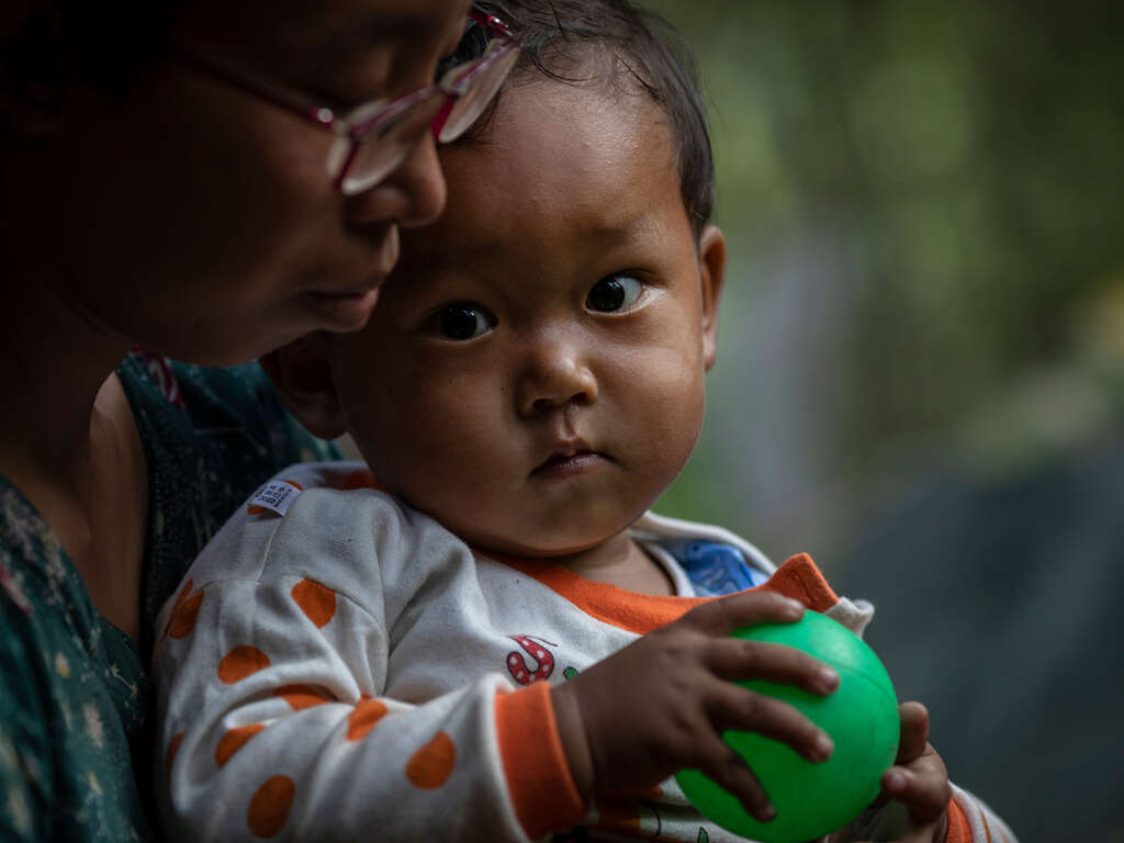 En liten pojke i Myanmar sitter i sin mammas knä.